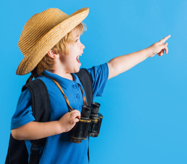 travel and adventure. happy kid boy with binoculars pointing finger at space for text. traveling child. advertising.